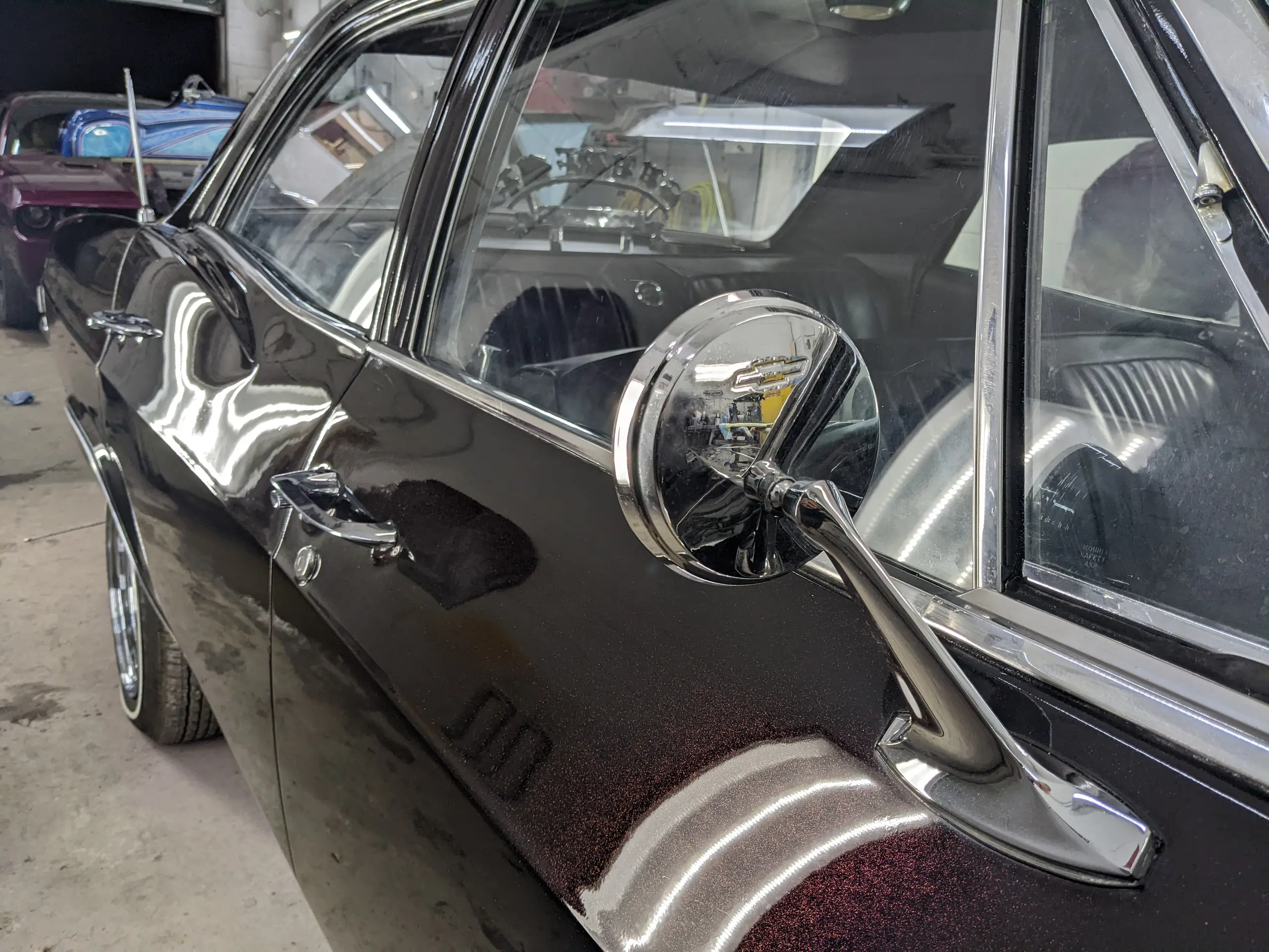 Reflets sur l’aile et le rétroviseur chromé d’une Chevrolet Impala noire à l’atelier SLM Auto