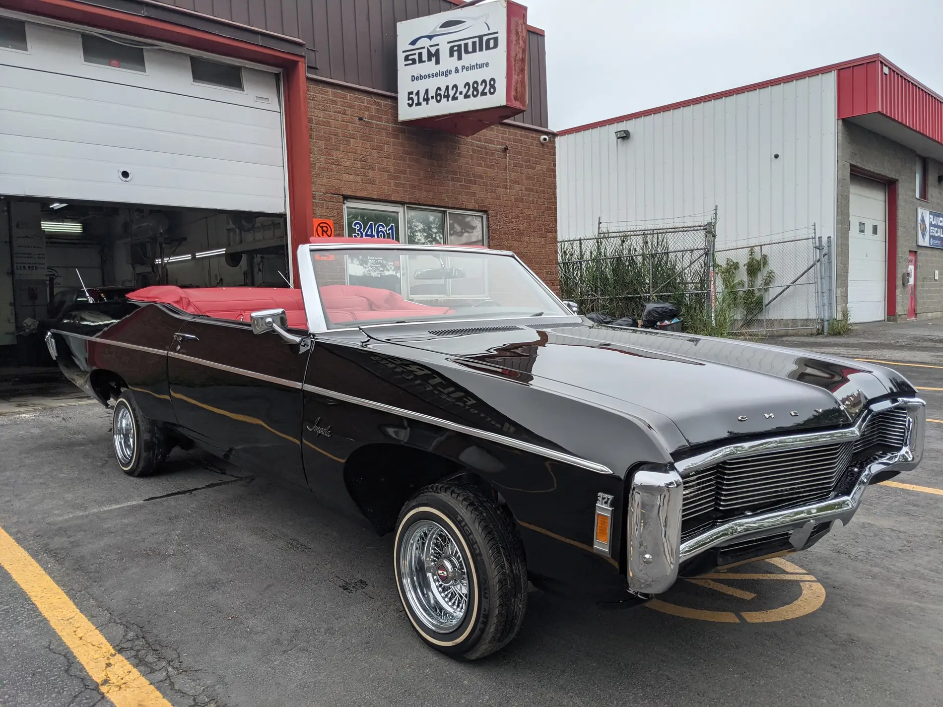 Chevrolet Impala noire décapotable devant l’atelier